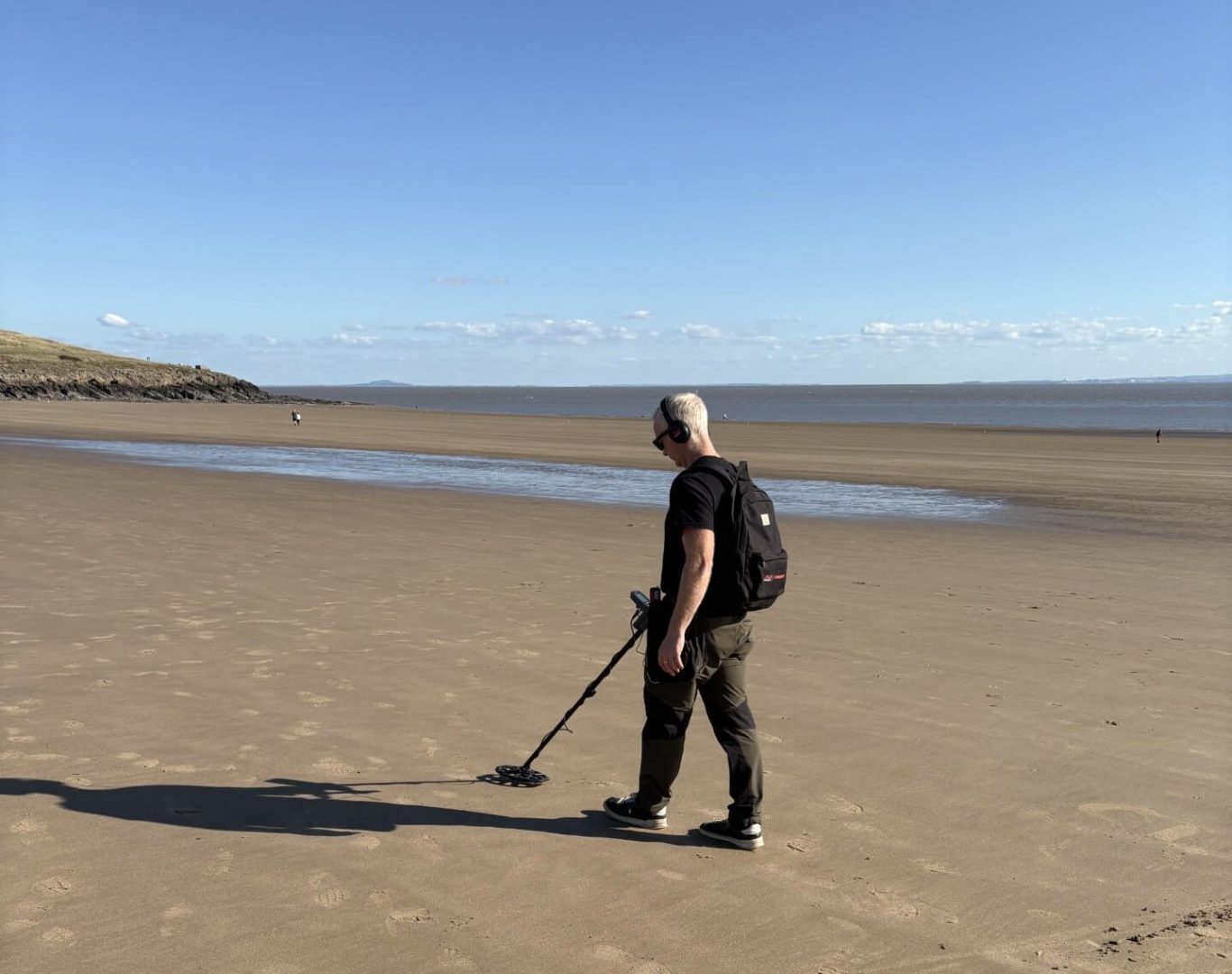 A person using a metal detector on a beach with water in the background.