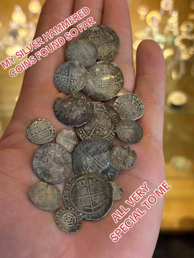 A hand holding a collection of old, silver hammered coins spread out.