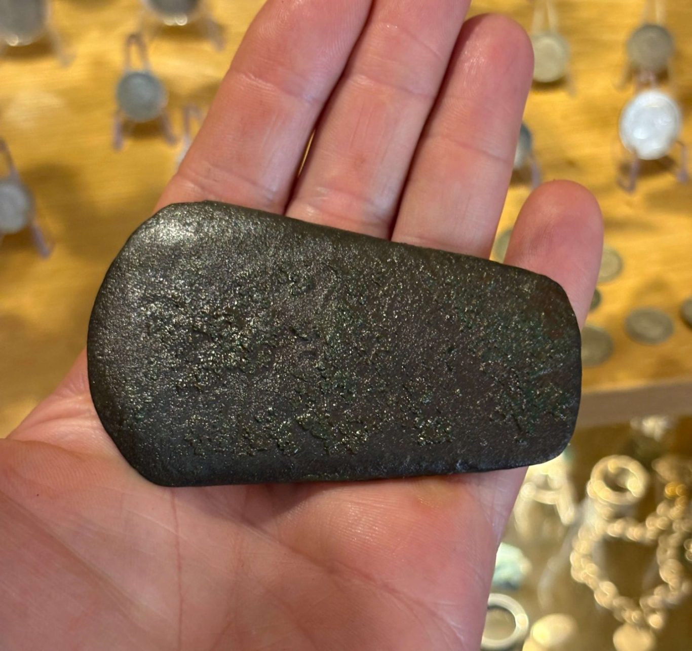 A hand holding a 4200 year old flat copper axe head, found metal detecting.